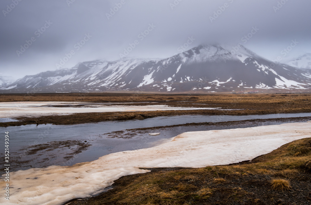 Meadow with snow and frozen lake and snowcapped mountains. Iceland