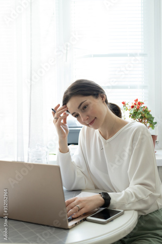 The smiling young girl e-learning with laptop in kitchen