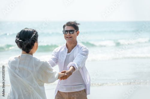 Smiling Asian senior couple holding hands together and looking at each other on tropical beach. Happy family retired old age man and woman relax and enjoy with romantic summer holiday vacation travel © CandyRetriever 