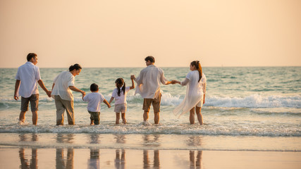 Happy multi generation Asian family holding hands and having fun together on tropical beach in summertime. Smiling big family parents with child boy and girl enjoy in summer lifestyle travel vacation