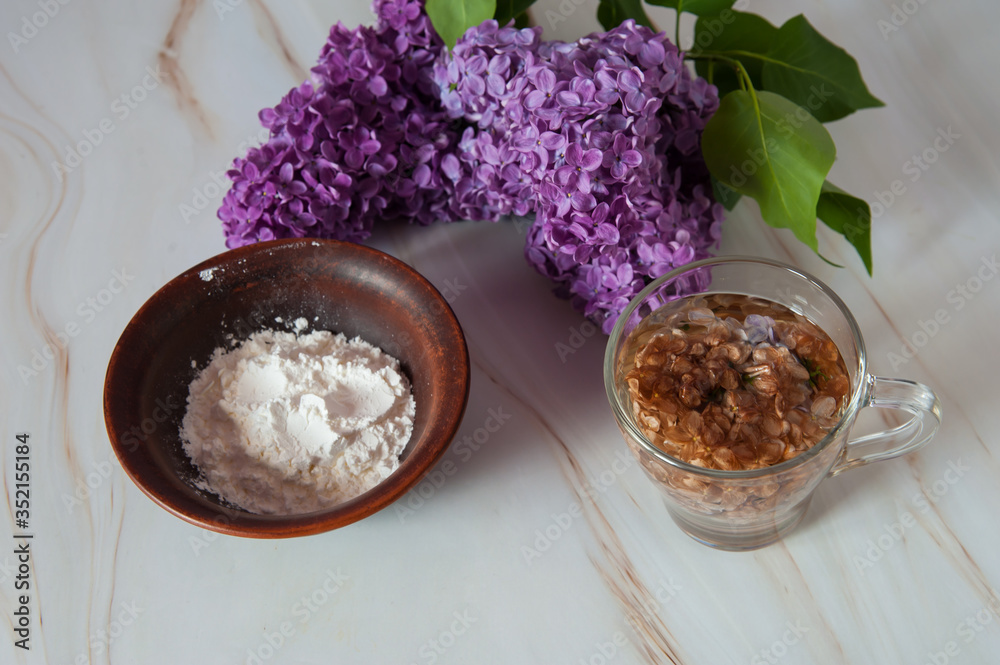 Natural home skin care. Ingredients of a face mask. Decoction of lilac flowers (Syringa vulgaris) and potato starch close-up on a marble background. Selective focus. Natural home skin care. Ingredients of a face mask. Decoction of lilac flowers (Syringa vulgaris) and potato starch close-up on a marble background. Selective focus.