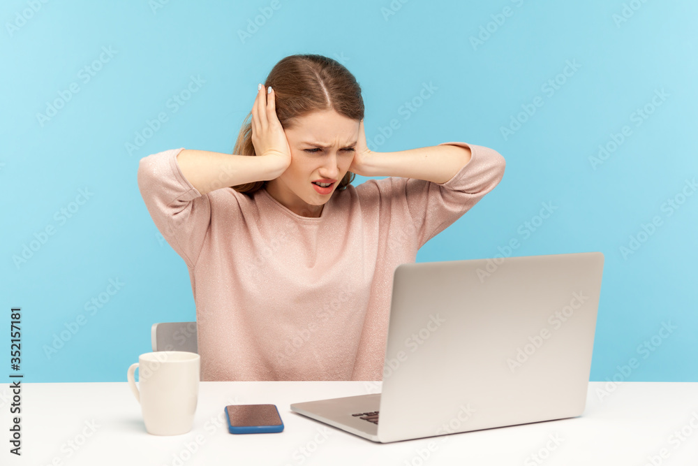Don't want to hear you. Angry woman employee covering ears and looking irritably at laptop screen, annoyed by unpleasant communication on video call. indoor studio shot isolated on blue background Don't want to hear you. Angry woman employee covering ears and looking irritably at laptop screen, annoyed by unpleasant communication on video call. indoor studio shot isolated on blue background
