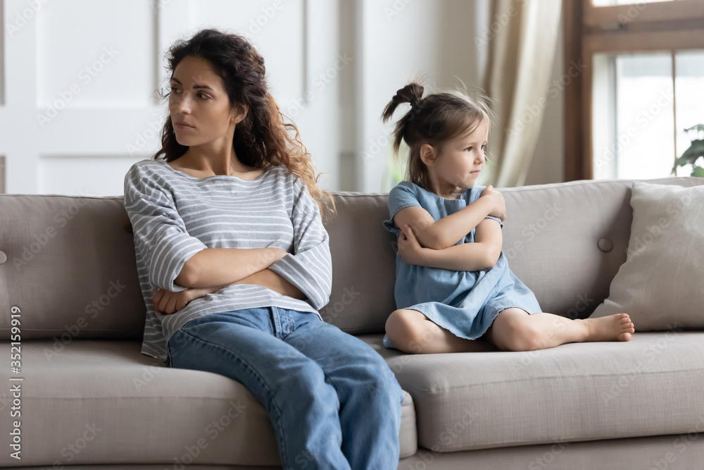 Angry depressed mother and stubborn little daughter ignoring each other after quarrel, pouting, sitting with arms crossed on couch in living room, parent and child, family generations conflict Angry depressed mother and stubborn little daughter ignoring each other after quarrel, pouting, sitting with arms crossed on couch in living room, parent and child, family generations conflict