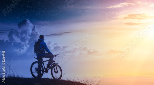 Cyclist on a mountain top between day and night