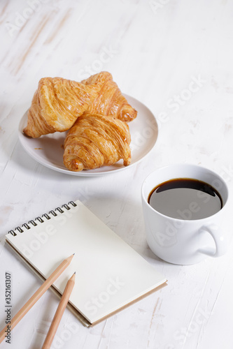 cup of hot coffee with croissant on white wooden background.  Working at home concept.