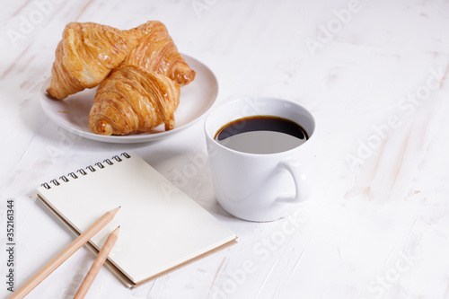 cup of hot coffee with croissant on white wooden background.  Working at home concept.