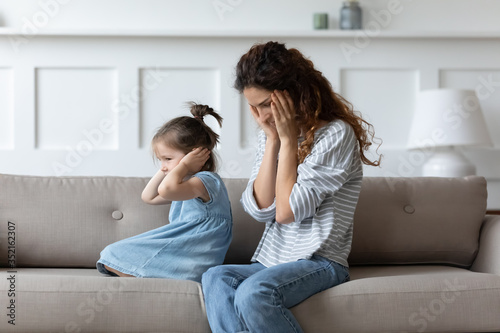 Stubborn spoiled little girl covering closing ears with hands, ignoring hopeless upset mother, parent and child, family generations conflict, complicated relationship between single mum and daughter