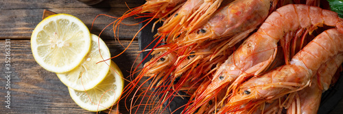 Large langoustines in a black metal basket on a brown wooden table. Seafood for a healthy diet. Banner 
