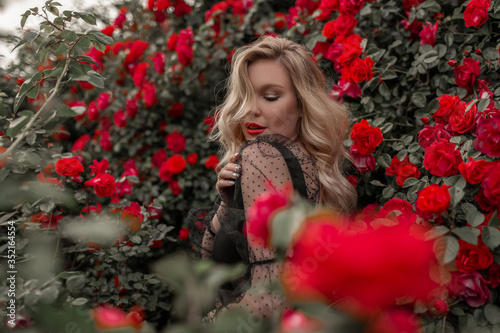 Beautiful blonde woman in garden with red roses.