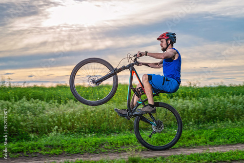 A cyclist in a helmet rides a bicycle on the rear wheel during sunset.