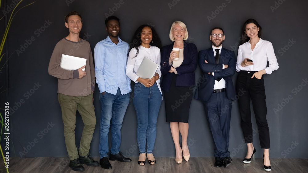 Fototapeta premium Smiling diverse business people standing in row on black wall background, successful happy employees team with leader boss looking at camera, staff posing for corporate portrait in office