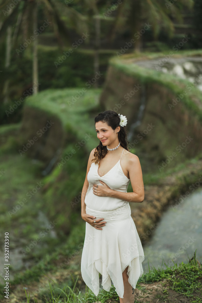 Young pregnant woman in white dress with view of Bali rice terraces in morning sunlight. Harmony with nature. Pregnancy concept. Young pregnant woman in white dress with view of Bali rice terraces in morning sunlight. Harmony with nature. Pregnancy concept.