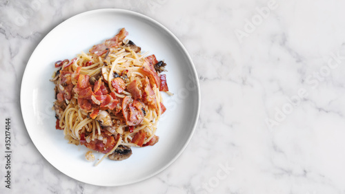 Stir fry Spaghetti bacon with Champion mushroom in white dish on white marble stone table top, with copy space