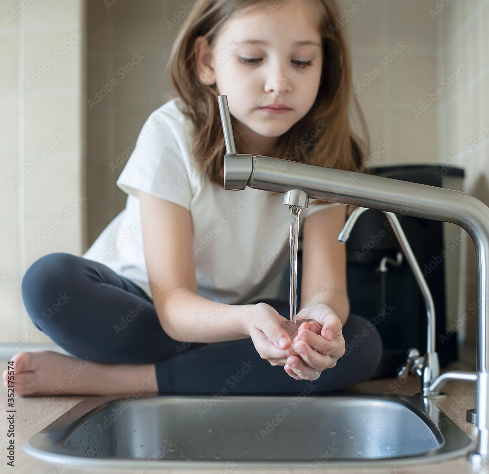 Child drinking water in kitchen at home. Thirsty baby. Hands open for