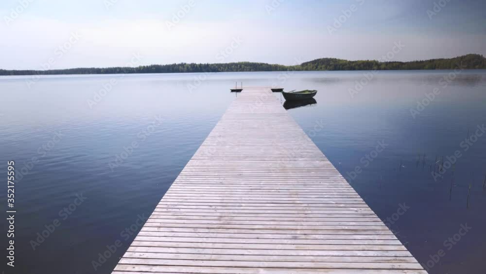 Passage on a wooden pier with a boat on the lake. The prospect goes to the horizon. Spring air is clear and the blue sky is clear. Latvia Passage on a wooden pier with a boat on the lake. The prospect goes to the horizon. Spring air is clear and the blue sky is clear. Latvia