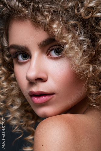 Cute cheerful woman close up portrait with afro curly hairstyle on a black background. Fresh, flawless skin