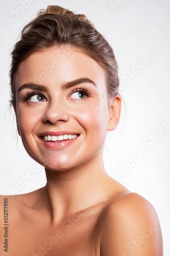 Close up of a brunette cute woman face with fresh clean flawless skin. She touches her face with her hand. Studio beauty portrait on white background