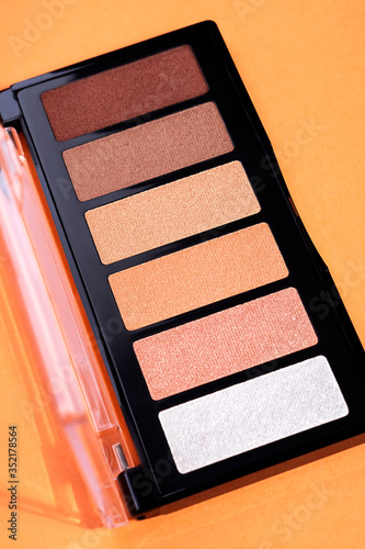 Professional colorful eye shadows for make up in plastic box on orange background. Space for text