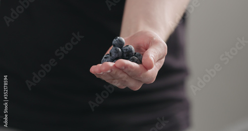 man hand show big ripe blueberries on neutral background