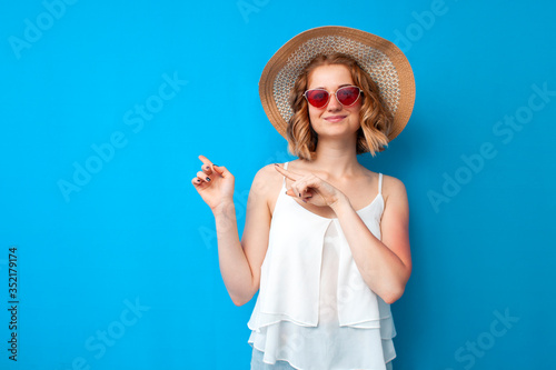 summer concept. cheerful girl in a sun hat and glasses shows a copy space on a blue isolated background, a woman advertises in summer clothes on vacation