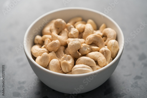 Dry cashew nuts in white bowl on concrete background closeup
