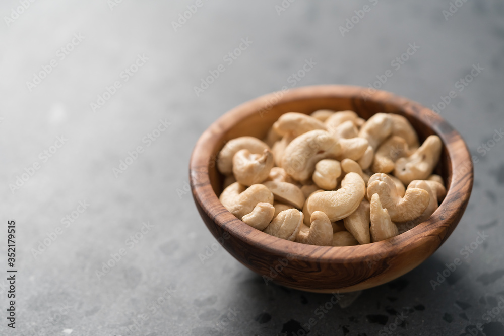 Dry cashew nuts in wood olive bowl on concrete background with copy space Dry cashew nuts in wood olive bowl on concrete background with copy space