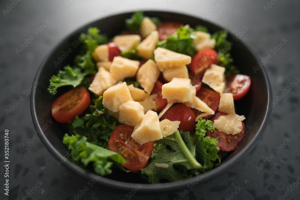 Salad with cherry tomatoes, kale and cheese in black bowl on concrete background Salad with cherry tomatoes, kale and cheese in black bowl on concrete background