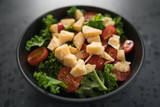 Salad with cherry tomatoes, kale and cheese in black bowl on concrete background