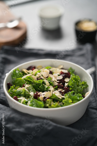 Salad with kale, cranberries and almond flakes in white bowl on linen napkin with copy space