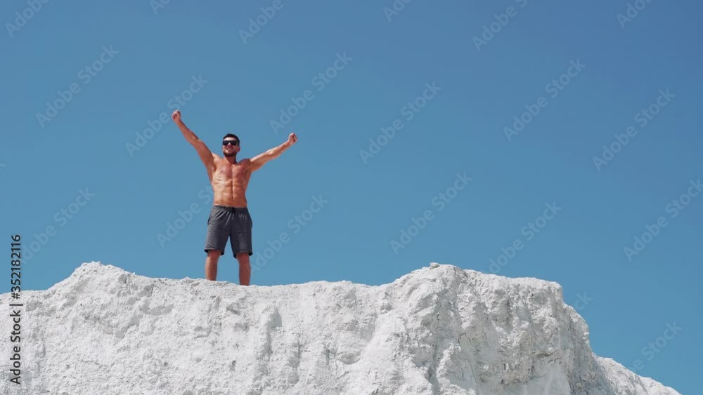 Male bodybuilder celebrates victory raising his arms high. Athlete in sunglasses on a white mountain. Male bodybuilder celebrates victory raising his arms high. Athlete in sunglasses on a white mountain.