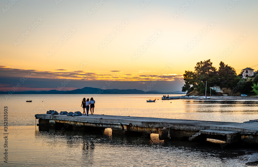 Three unidentified young girls enjoy a scenic sunset in Afissos, Greece.