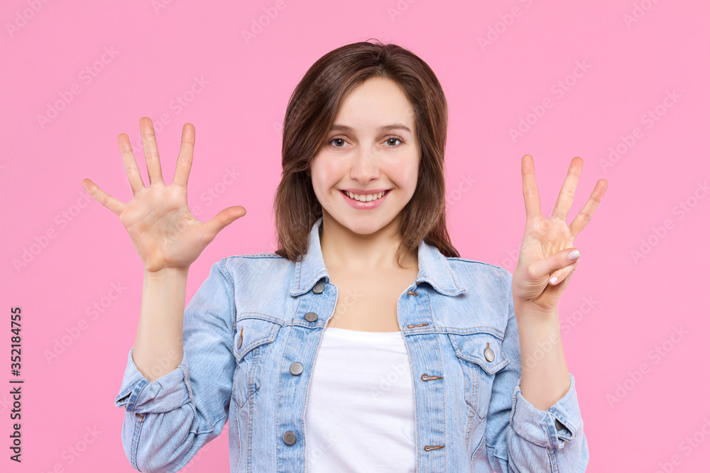 Cheerful smiling girl dressed in white t-shirt, denim jacket on pink background. Young woman is showing with fingers number eight, percents, discount. Female gesturing. Emotional portrait concept. Cheerful smiling girl dressed in white t-shirt, denim jacket on pink background. Young woman is showing with fingers number eight, percents, discount. Female gesturing. Emotional portrait concept.
