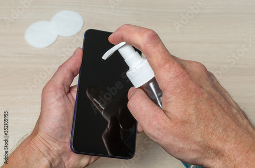 A man disinfects the screen of his mobile phone using antiseptic and cotton pads