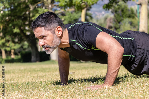 Sportsman doing pushups and exercising outdoors. Athletic man with a white beard doing workout in the park.