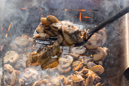 juicy appetising champignons are cooking on grill or BBQ steam. The cook mixes the mushrooms with a kitchen spatula. Selective focus. Food background. Delicious healthy meals for vegetarians.