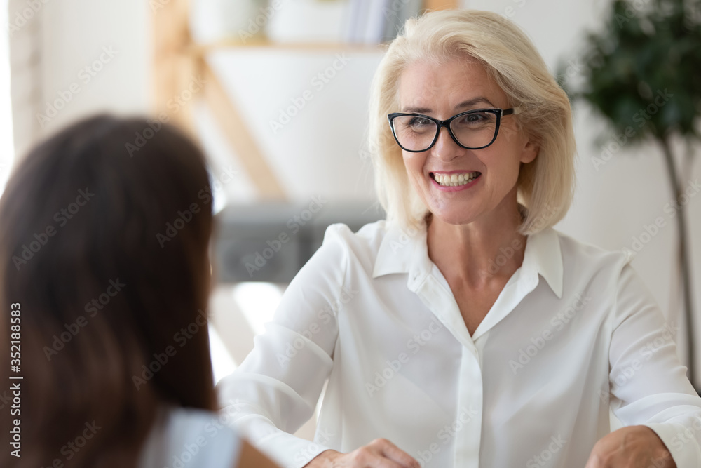 Smiling middle-aged businesswoman talk with female business client or partner at meeting, happy excited senior woman employer or boss speak with applicant at interview in office, recruitment concept Smiling middle-aged businesswoman talk with female business client or partner at meeting, happy excited senior woman employer or boss speak with applicant at interview in office, recruitment concept