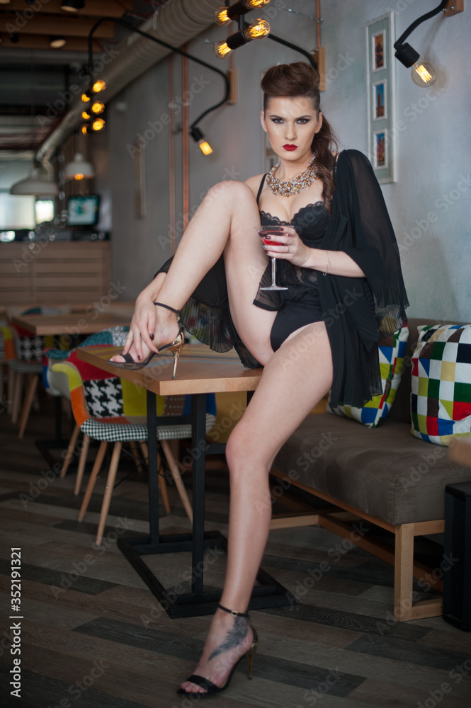 Sensual girl with long legs and high heels sitting on the chair in bar drinking .Handsome girl wearing beautiful body and high heels in indoor scene.Fashion model with long sexy legs drink cocktail.