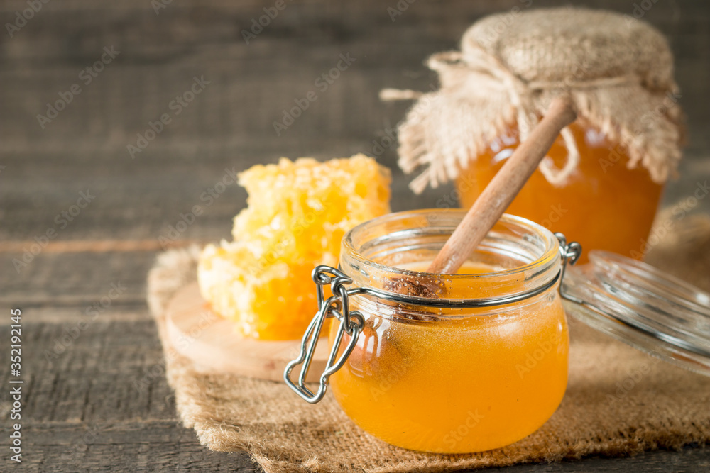 Honey dripping from a wooden honey dipper in a jar on wooden grey rustic background Honey dripping from a wooden honey dipper in a jar on wooden grey rustic background
