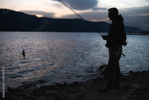 Man fishing on mountain lake. Sunrise low light.