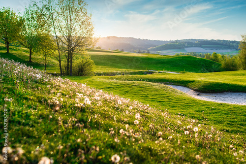 spring looking grassland  small gold course and flowers with sunrays in the sunrise