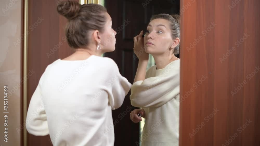 woman paints eyelashes in front of a mirror at home, going to a meeting or to work or on a date woman paints eyelashes in front of a mirror at home, going to a meeting or to work or on a date