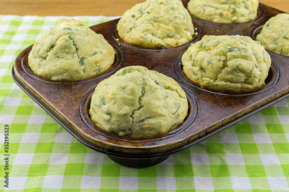 Freshly baked feta cheese and spinach muffins in a muffin pan on green and white check table cloth Freshly baked feta cheese and spinach muffins in a muffin pan on green and white check table cloth