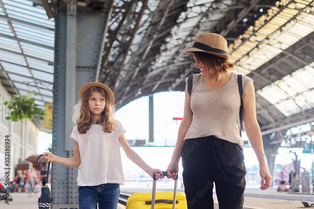 Happy mother and daughter child walking together at railway station with suitcase Happy mother and daughter child walking together at railway station with suitcase