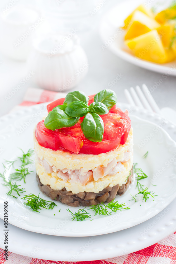 Festive layered salad with fried champignons, smoked chicken, eggs and cheese, garnished with fresh tomatoes, selective focus Festive layered salad with fried champignons, smoked chicken, eggs and cheese, garnished with fresh tomatoes, selective focus