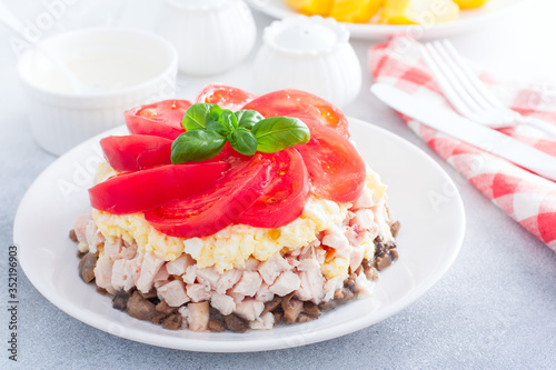 Festive layered salad with fried champignons, smoked chicken, eggs and cheese, garnished with fresh tomatoes, selective focus
