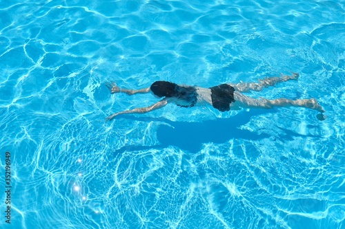 Young woman in bikini swimming underwater in an outdoor swimming pool  top view