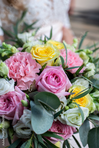 close up bride s bouquet of roses  pink  yellow  white   the bride holds a bouquet of flowers in her hands  vertically 