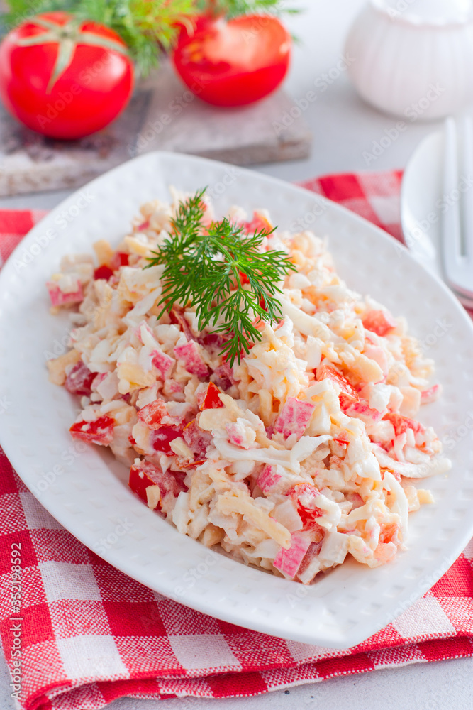 salad with crab sticks, tomatoes, cheese on a white dish, selective focus