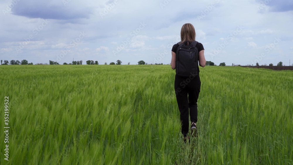 A tourist walks on a wheat field with a backpack on her shoulders.