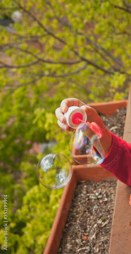 child's hand making soap bubbles, blurred background and vertical format
